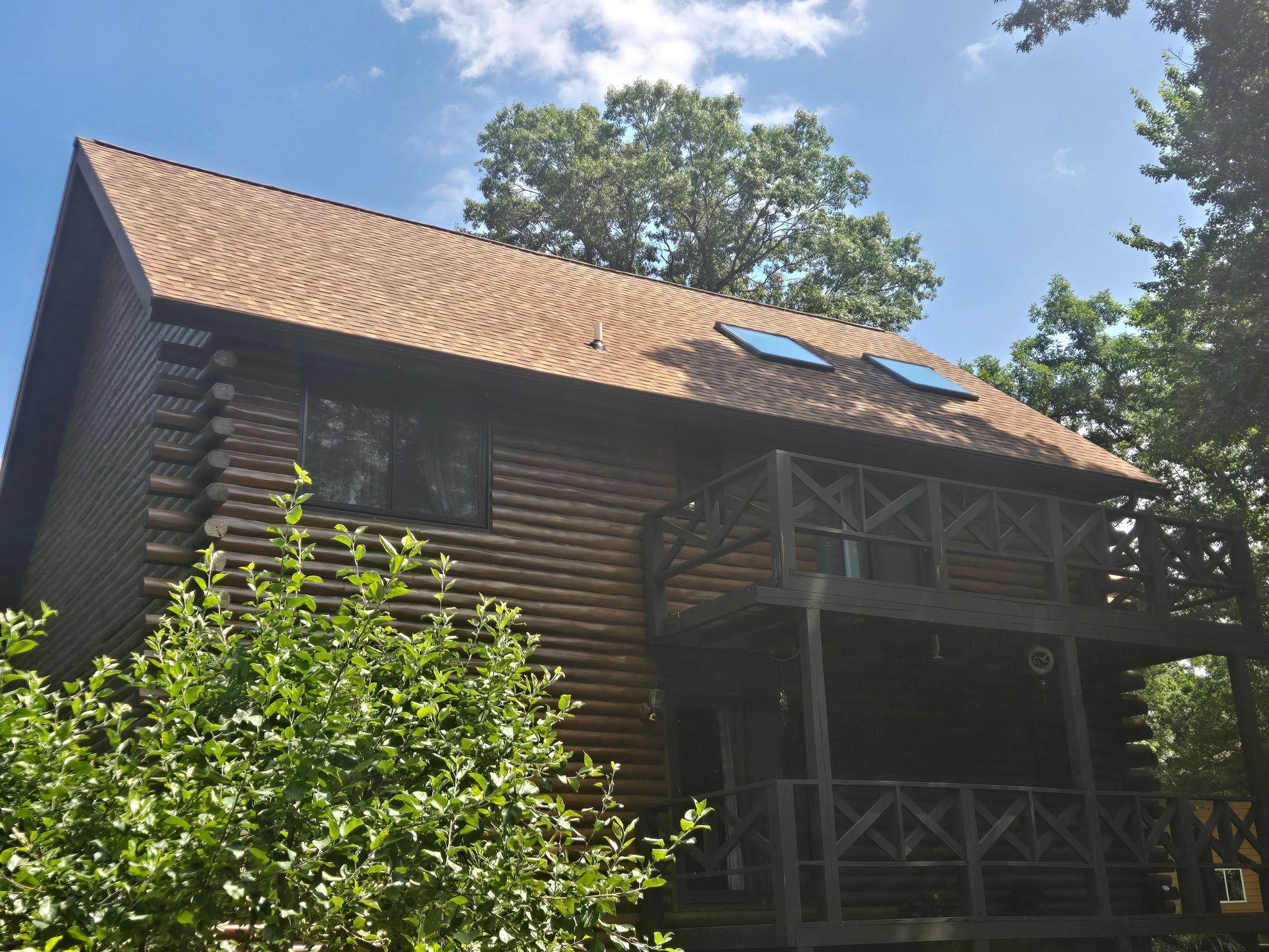 Wooden cabin with a steep roof and balcony, surrounded by trees under a bright blue sky