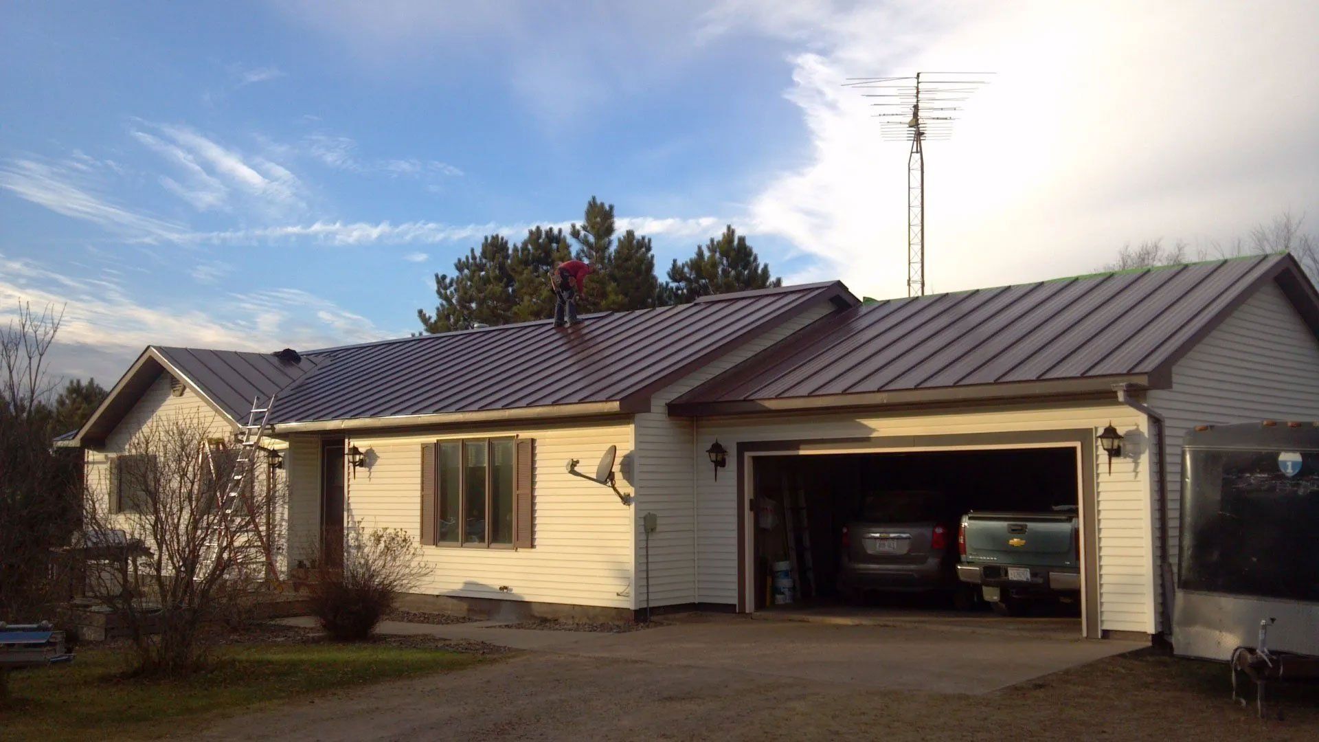 Single-story house with a gray metal roof and an open garage driveway at sunset