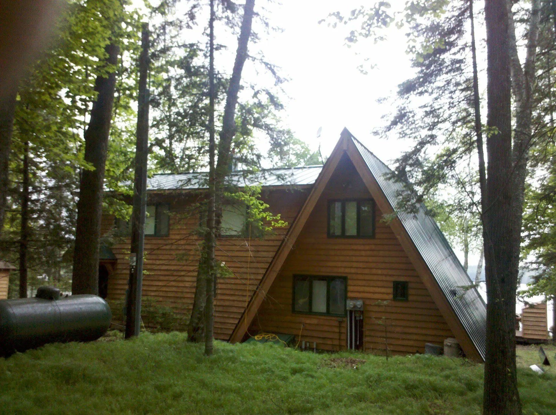 A-frame cabin with wood siding in a pine forest, seen through tall trees and green grass.