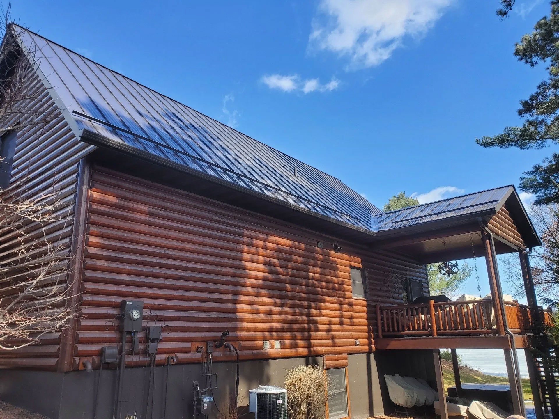 Wooden log cabin with a steep metal roof and covered porch under a blue sky