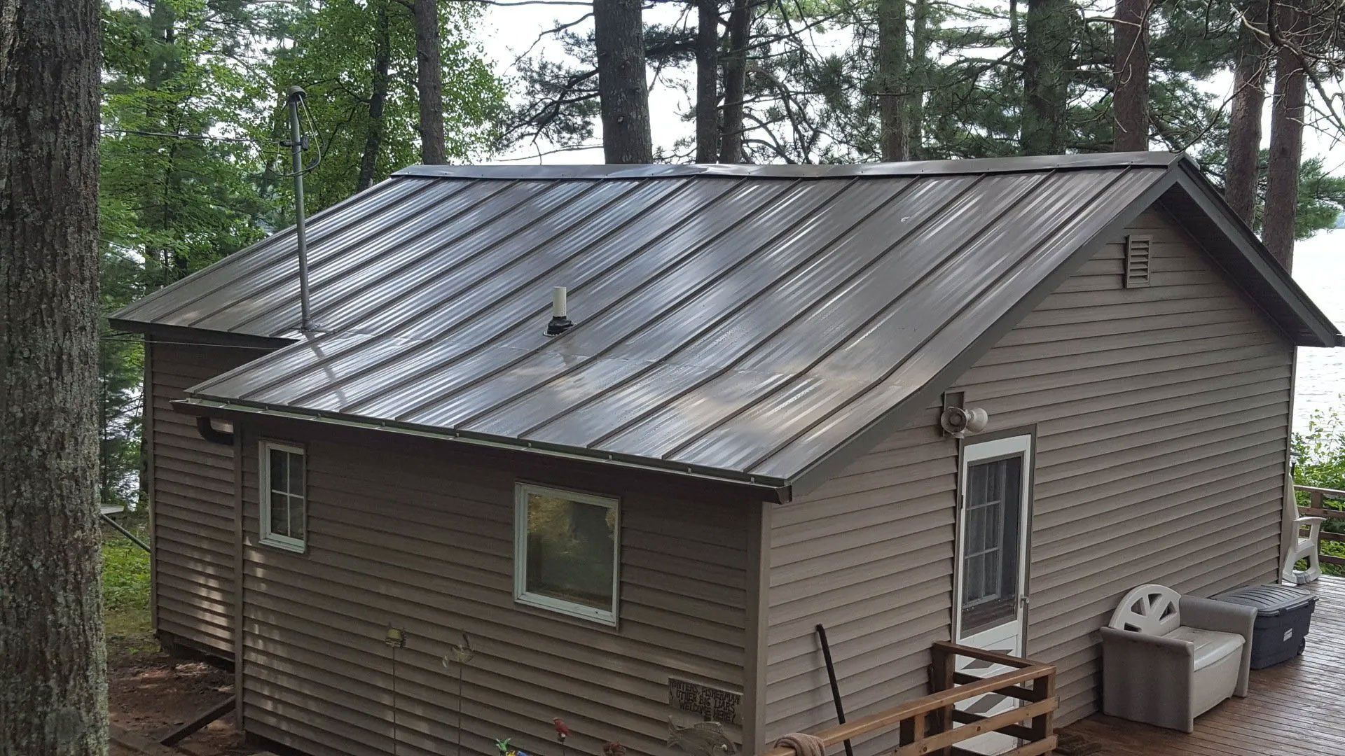 Small brown cabin with metal roof in a wooded area, viewed from above.