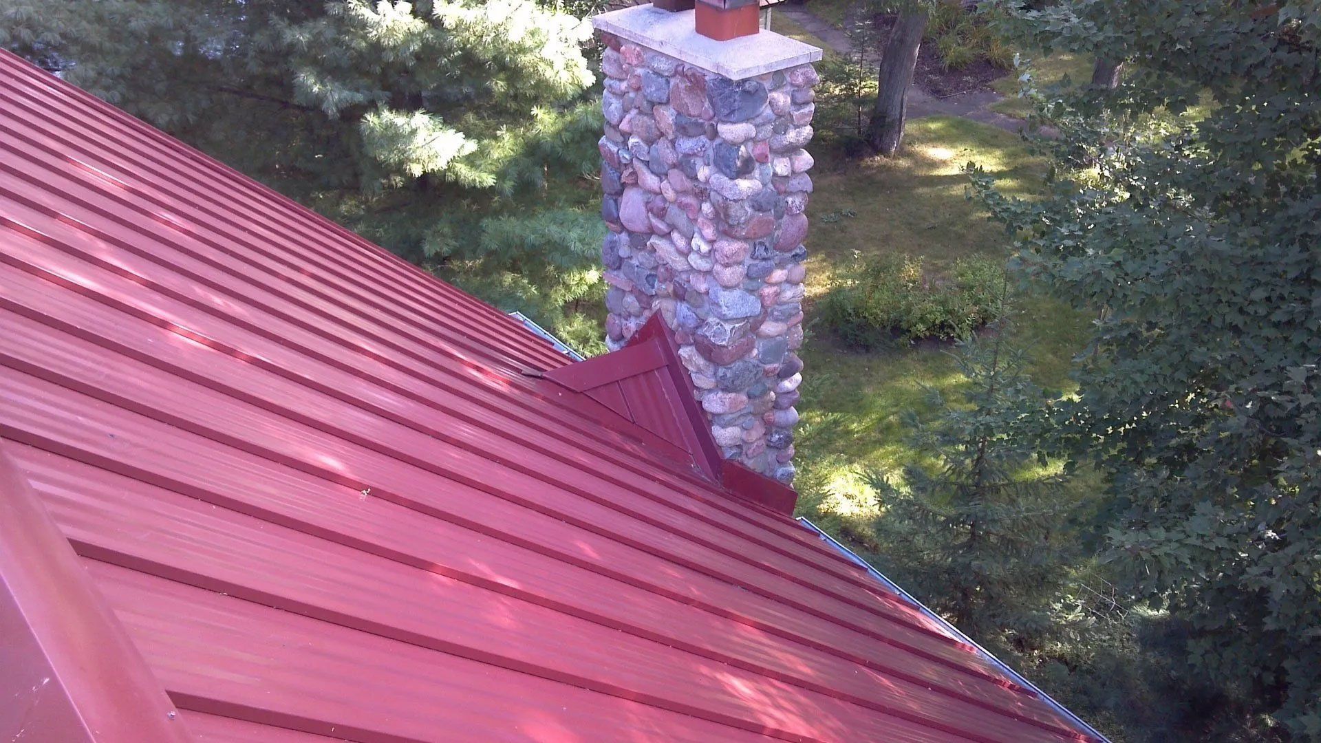 Red metal roof beside a stone chimney amid green trees
