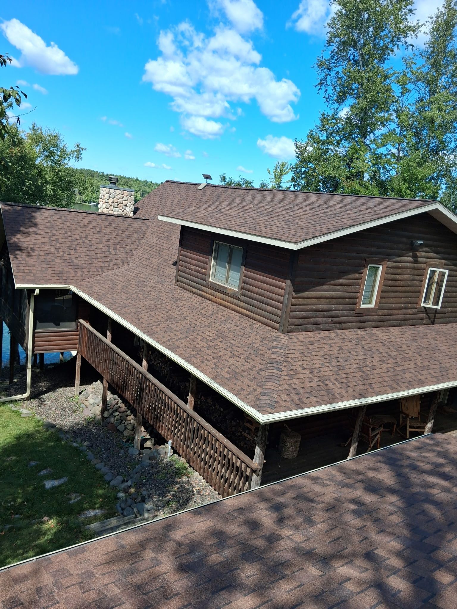 Brown shingled house with a sloped roof under a bright blue sky with clouds