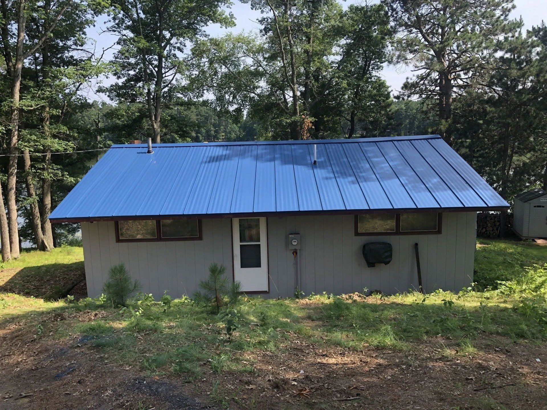 Small gray house with a blue metal roof in a wooded clearing
