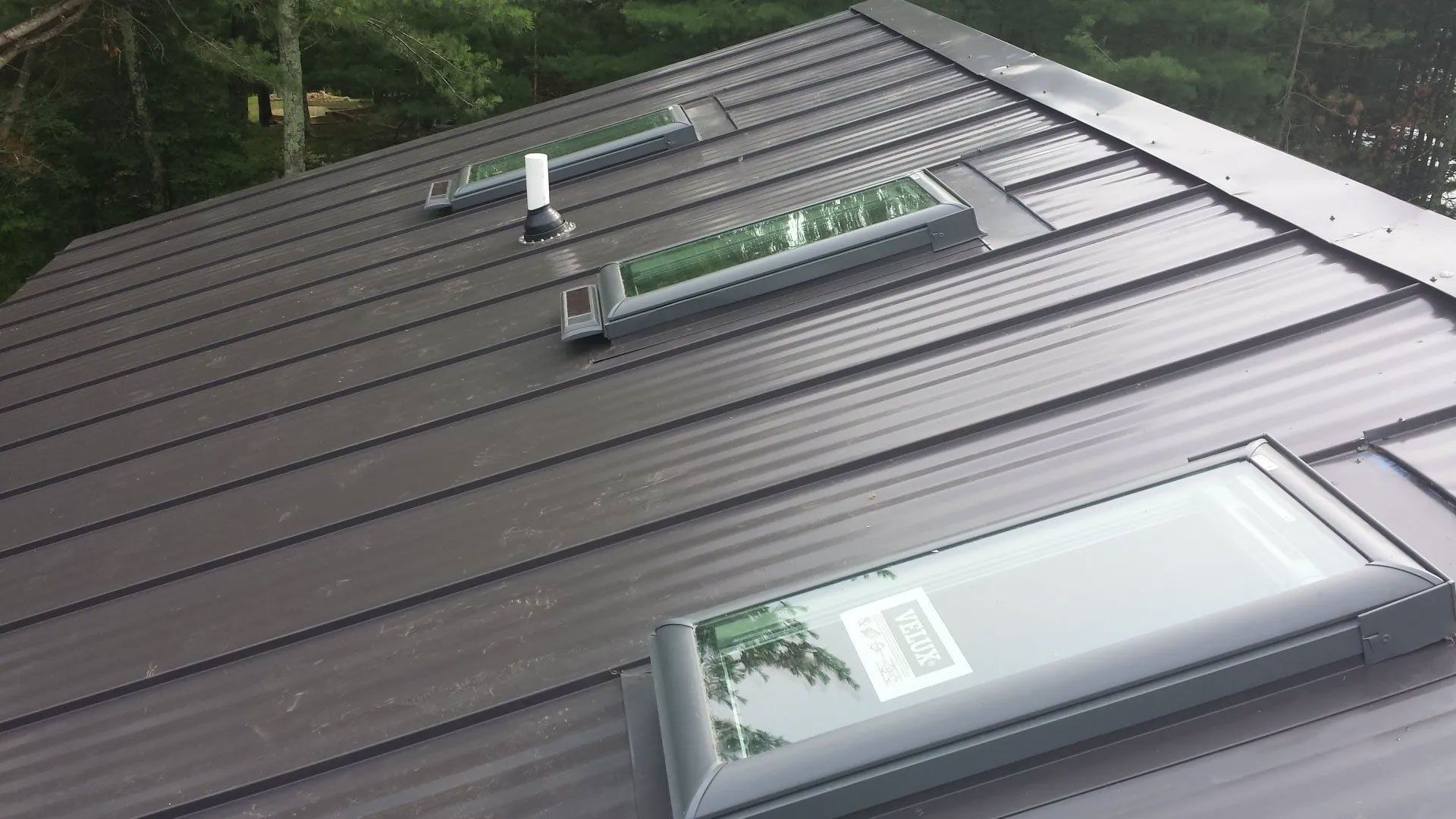 Dark metal roof with three skylights, viewed from above.