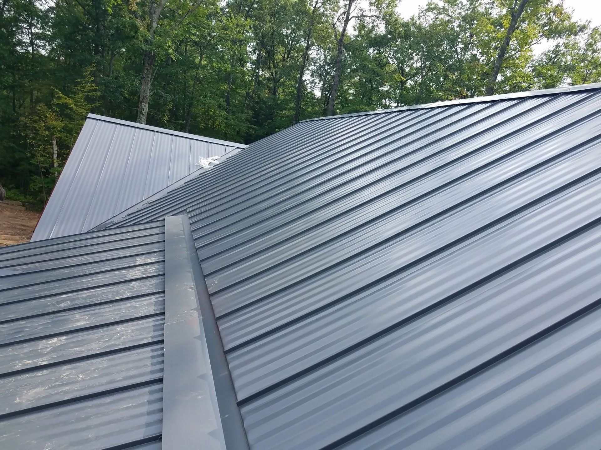 Gray metal roof with standing seams on a house, surrounded by trees