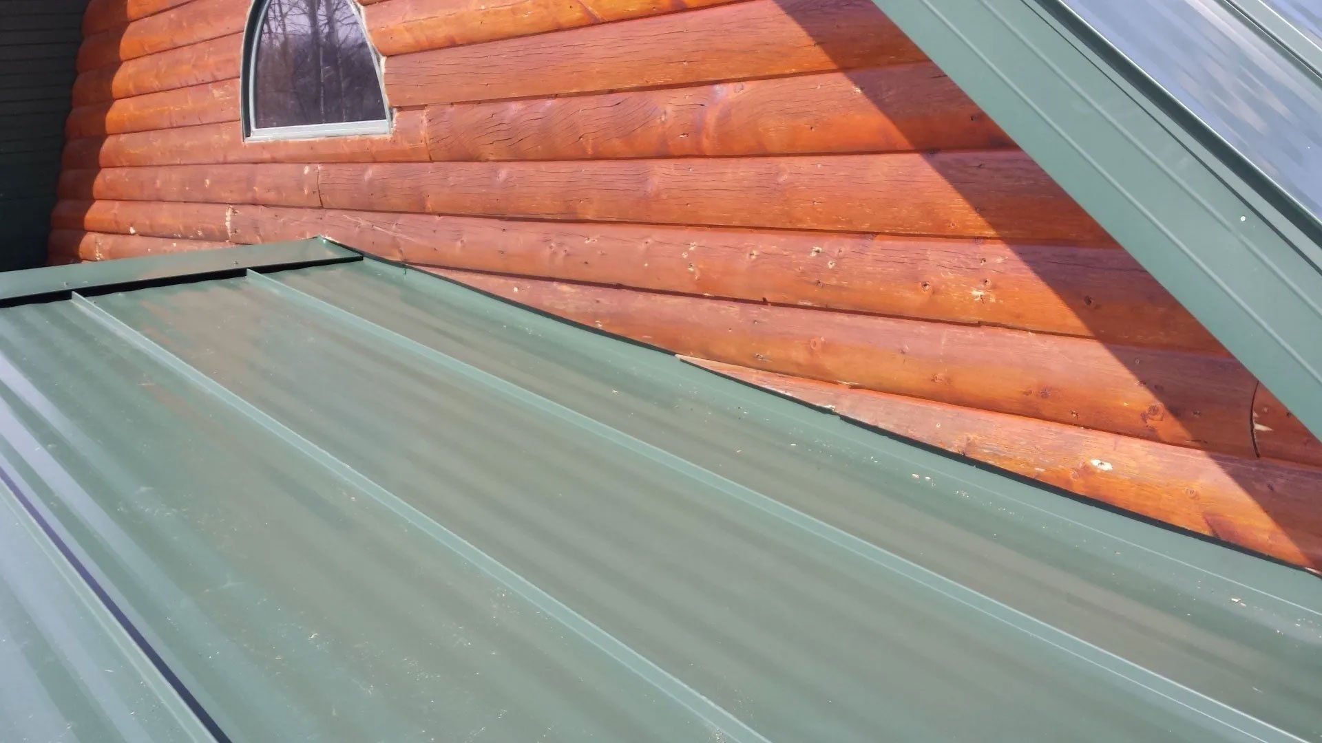 Green metal roof beside a red wooden wall with a small arched window