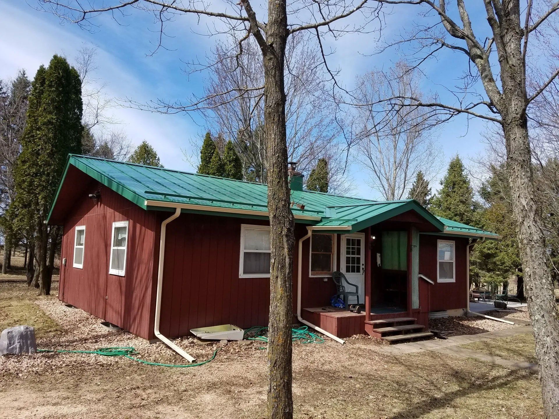 Small red cabin with green roof in a wooded area under a blue sky