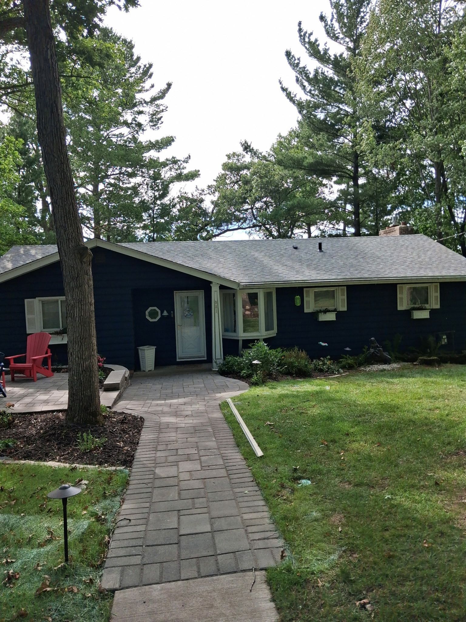 Single-story blue house with a brick walkway, trees, and a lawn in front.