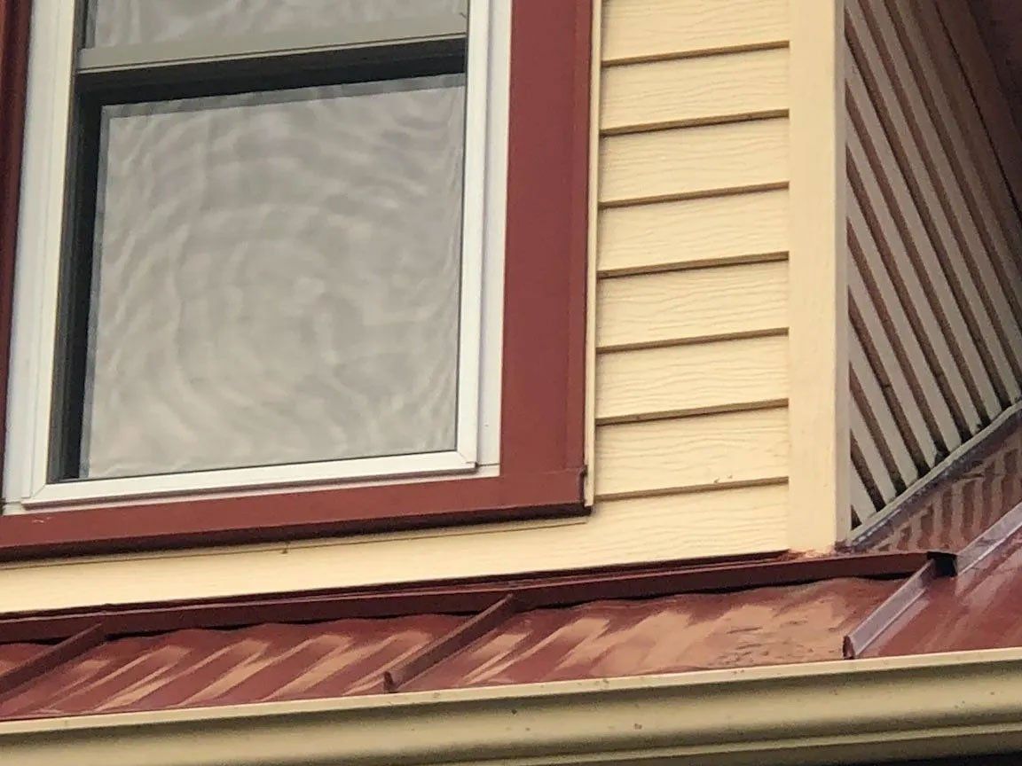House exterior with beige siding, maroon window trim, and a rust-colored metal roof.