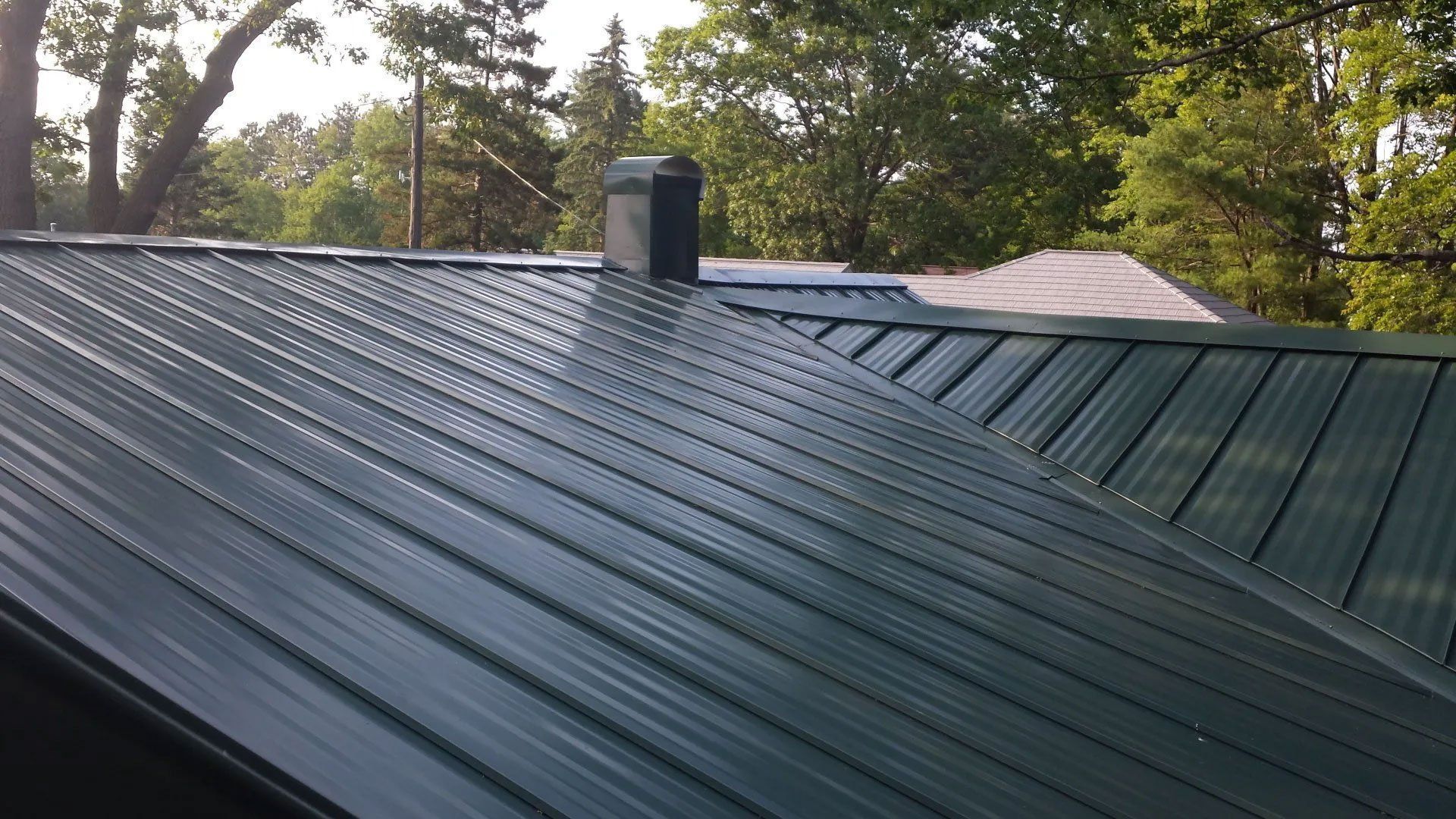 Green metal roof with a chimney, viewed from above with trees in the background