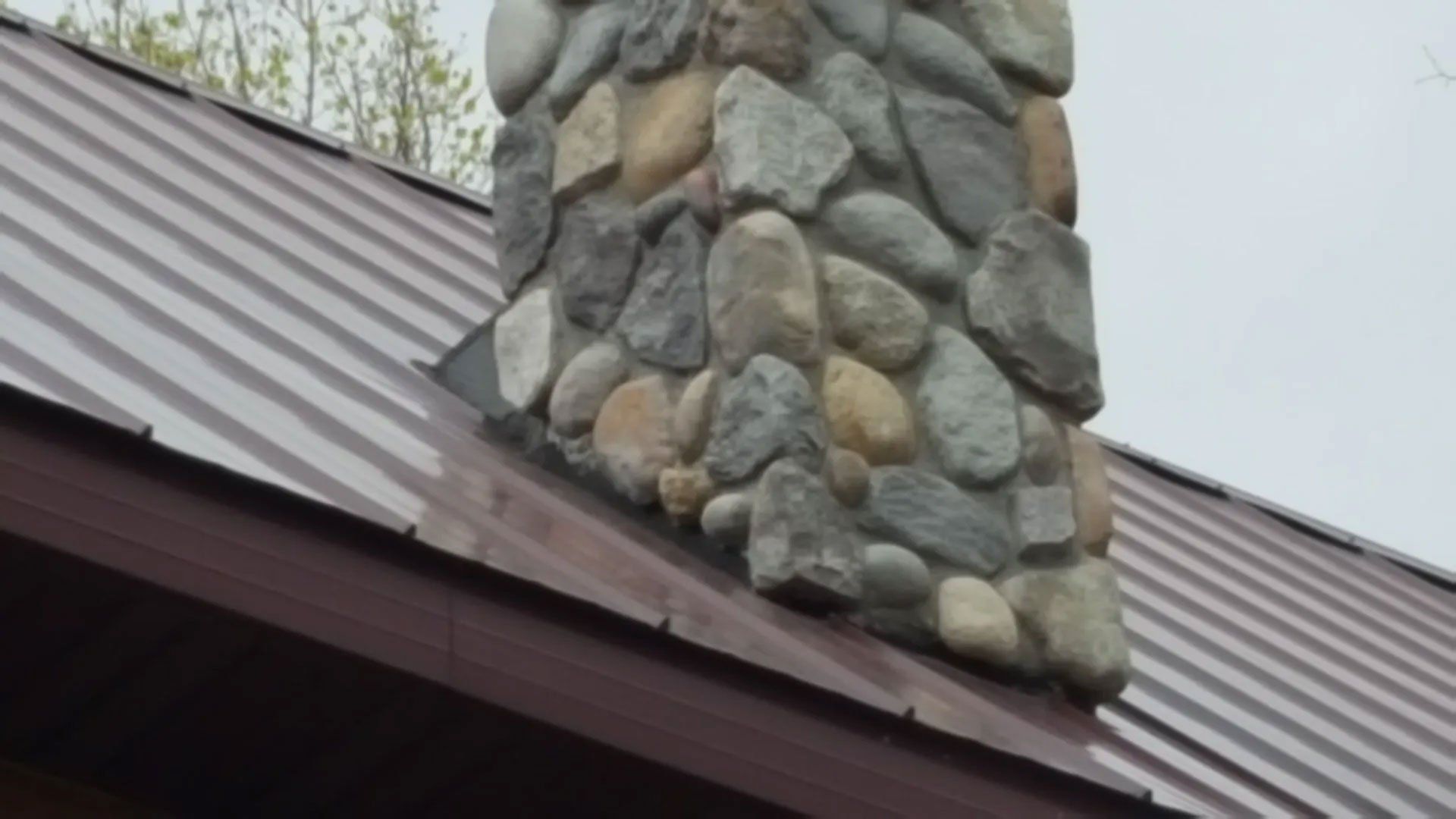 Stone chimney on a dark metal roof against a cloudy sky