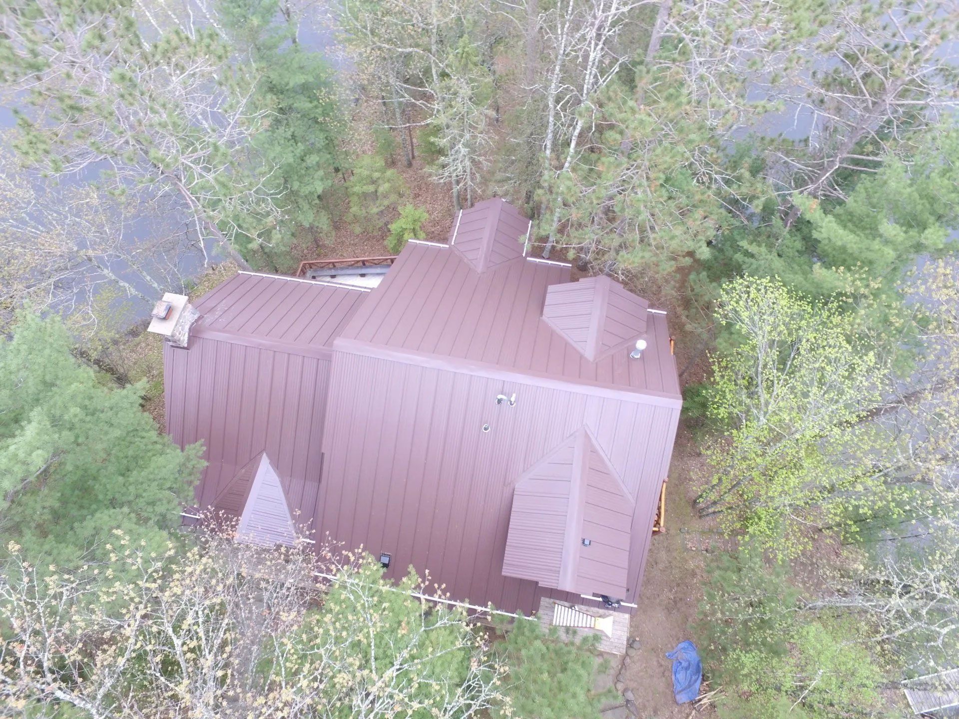 Aerial view of a brown house roof surrounded by dense green trees.