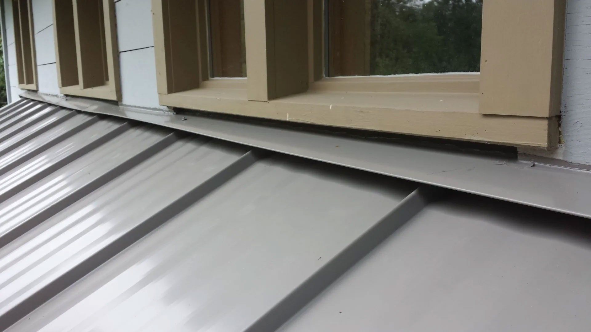 Metal roof edge beneath beige window trim and siding on a house exterior.