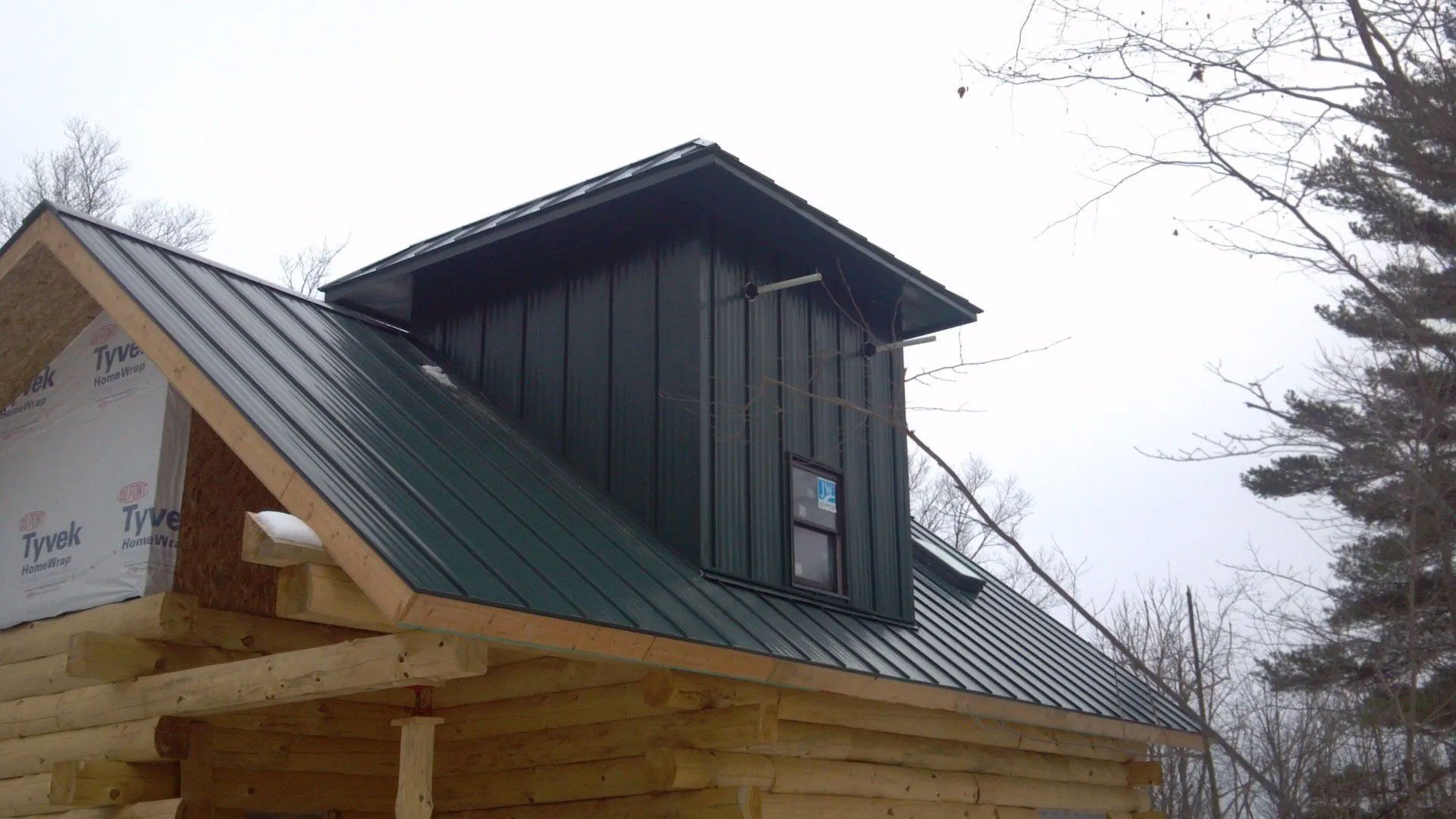 Partially finished house with green metal roof and dark dormer under construction outdoors