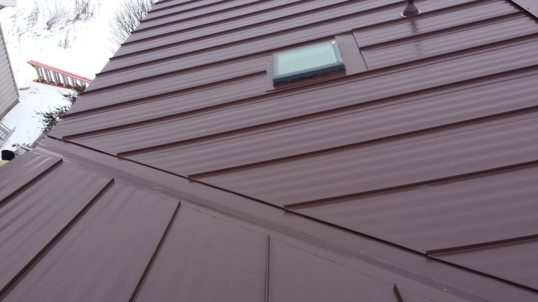 Brown metal roof with a small skylight, viewed from below against a pale sky.