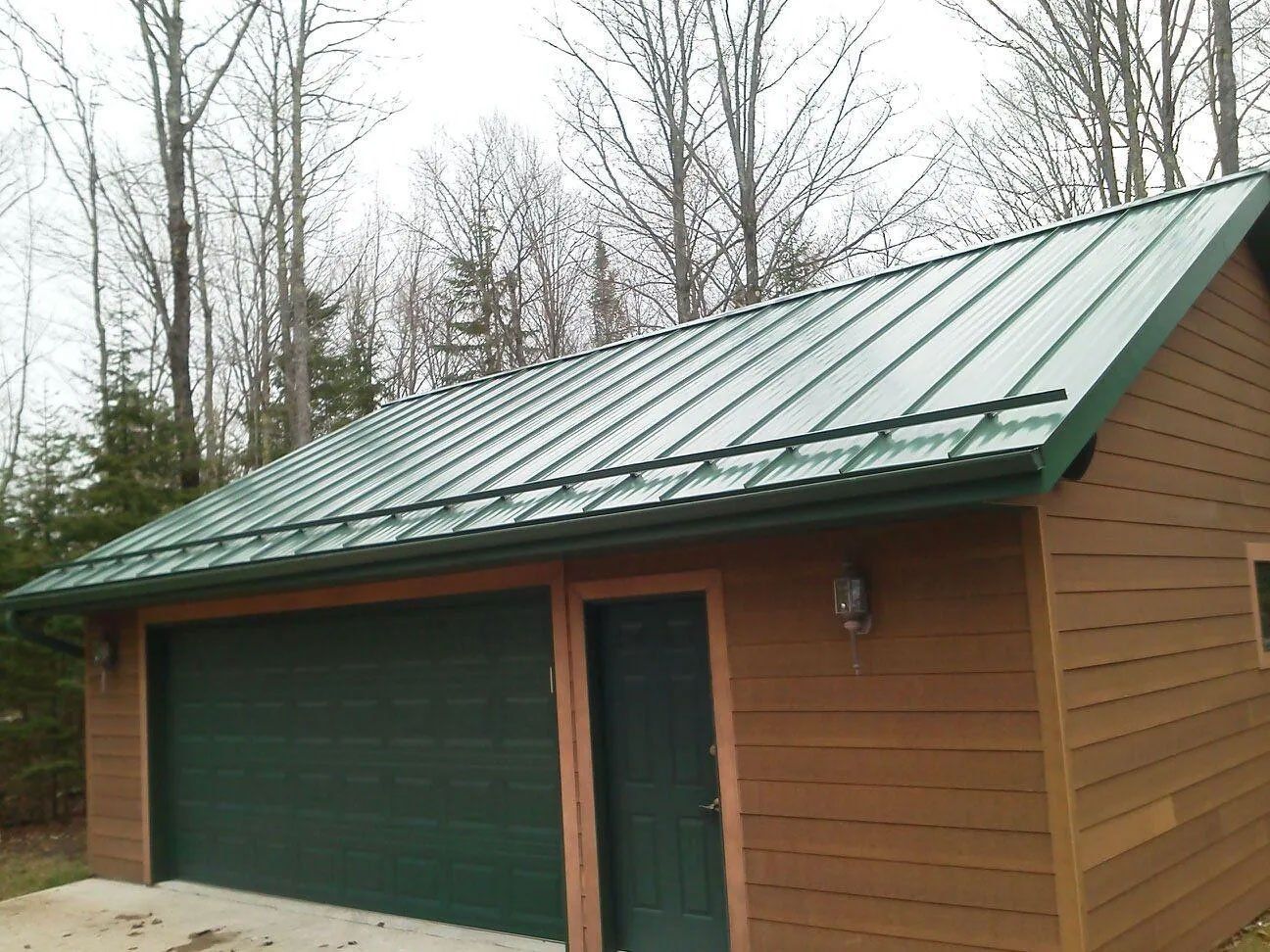 Green-roofed wooden garage with a green door, set among leafless trees