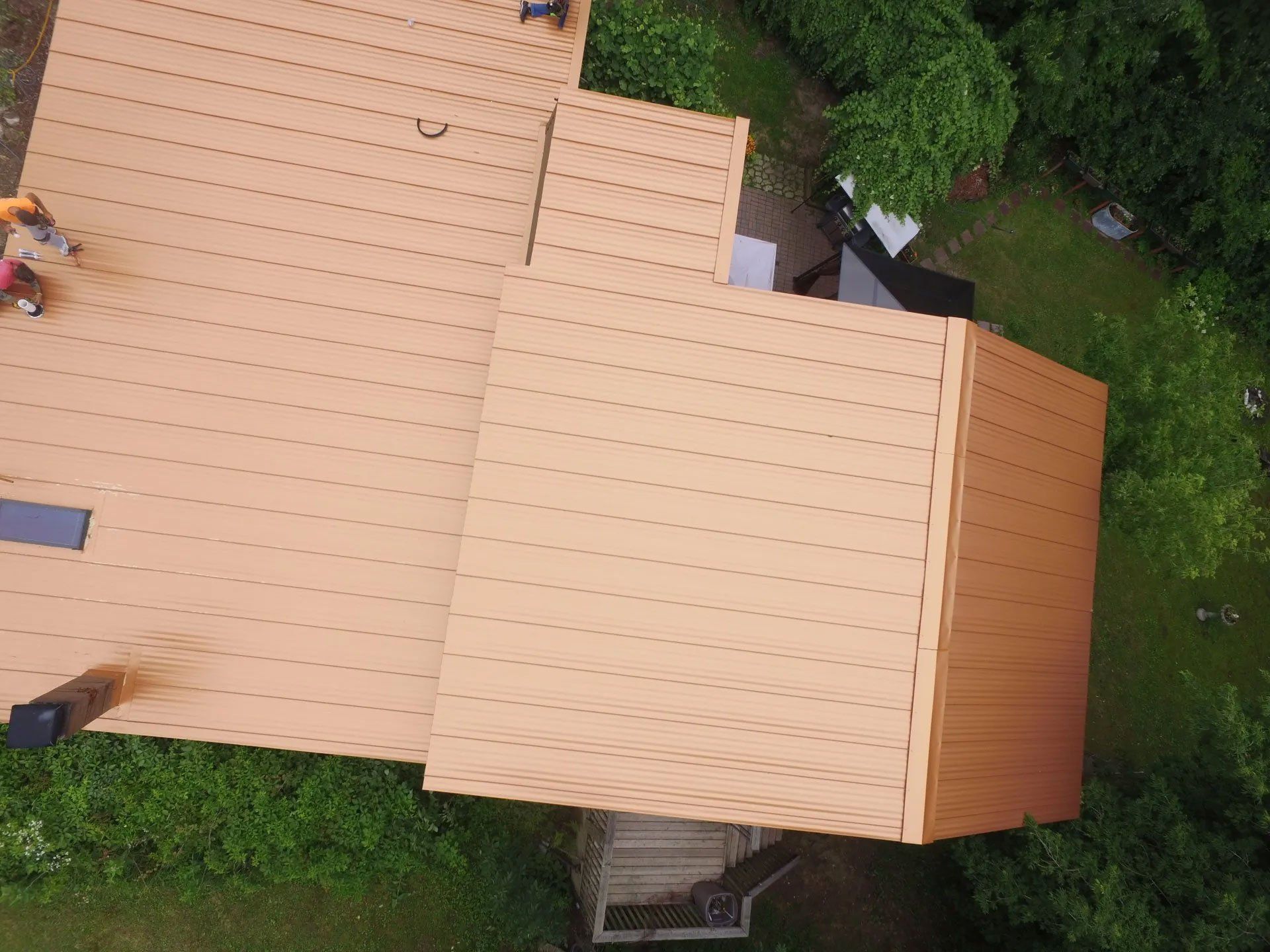 Top-down view of a tan roof surrounded by green trees and shrubs