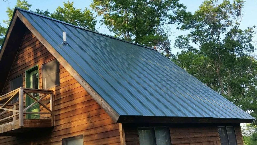 Wooden cabin with a steep metal roof and a small balcony, surrounded by trees
