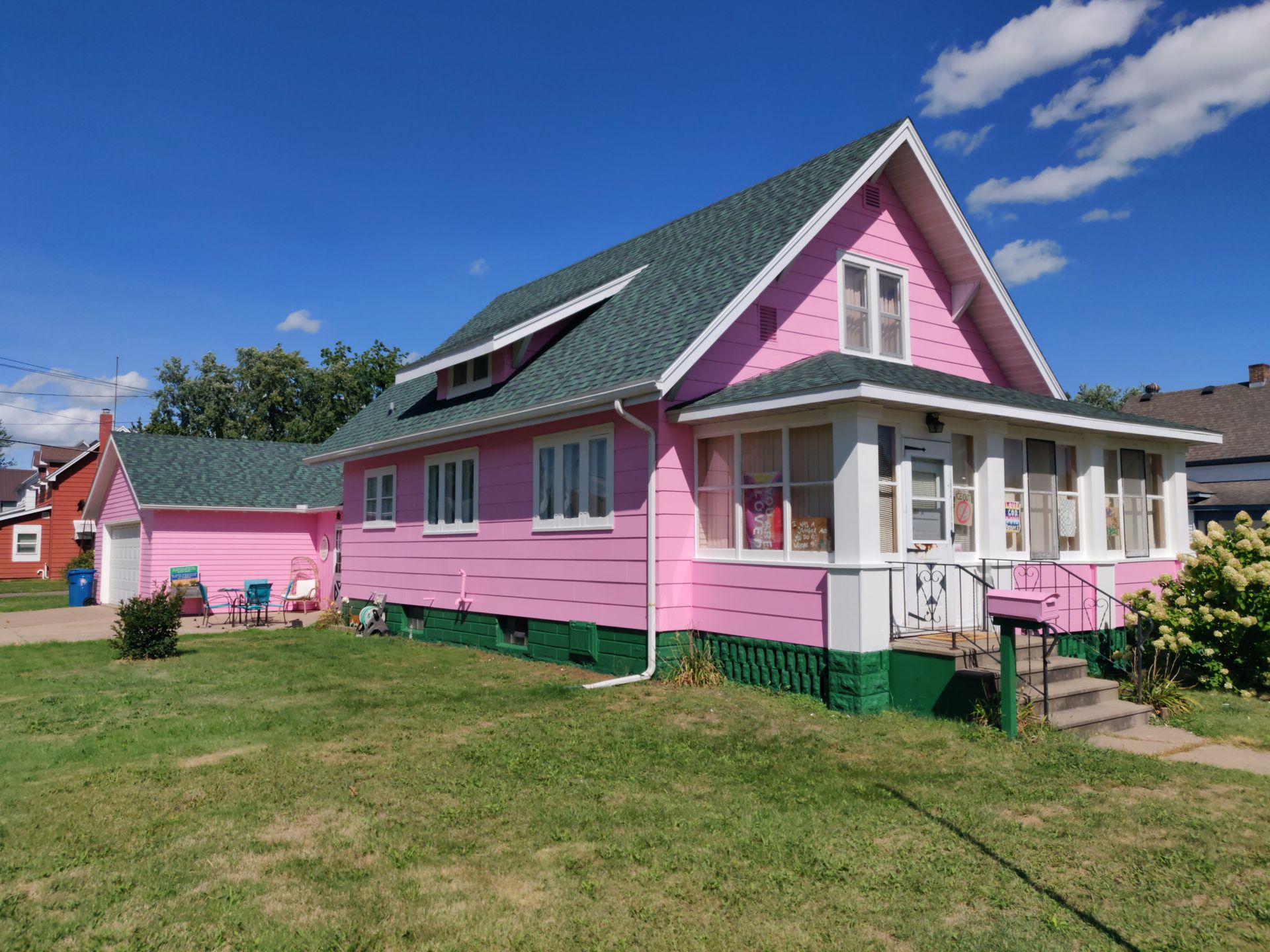 Pink house with white trim and porch under a blue sky, viewed from a grassy yard