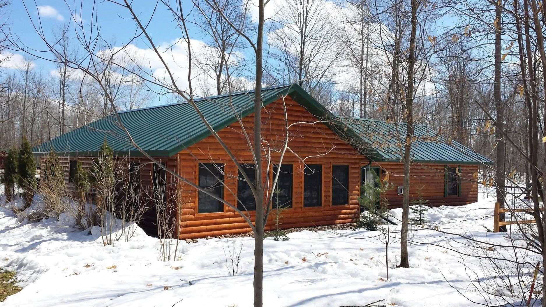 Snowy woodland cabin with green roof and orange log walls among leafless trees