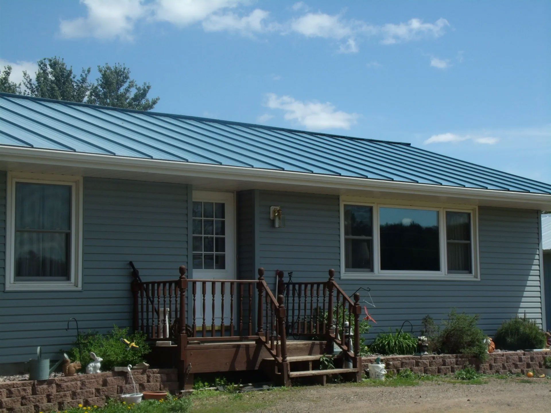 Blue house exterior with a front porch, steps, and flower beds under a clear sky