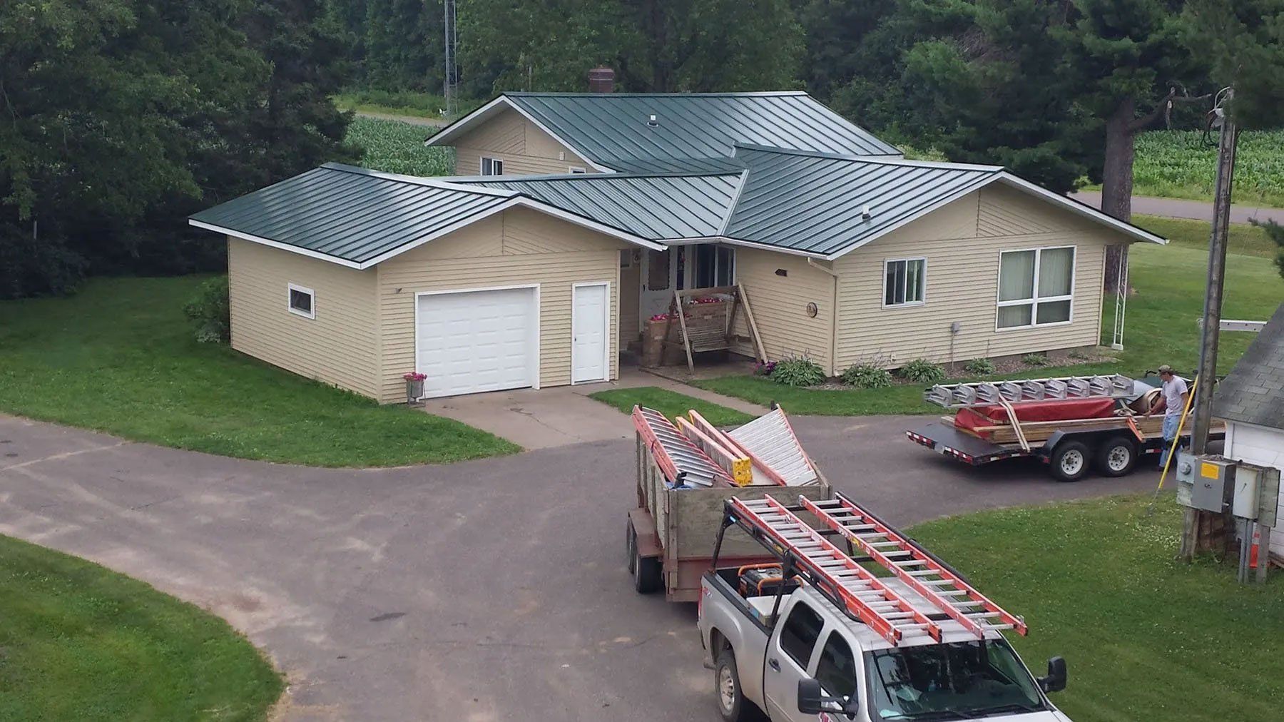House with green roof and parked utility trucks in driveway, viewed from above