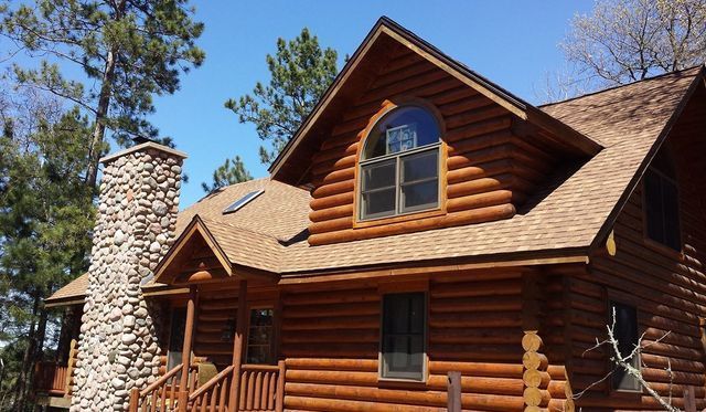 Log cabin with stone chimney and log porch beneath pine trees
