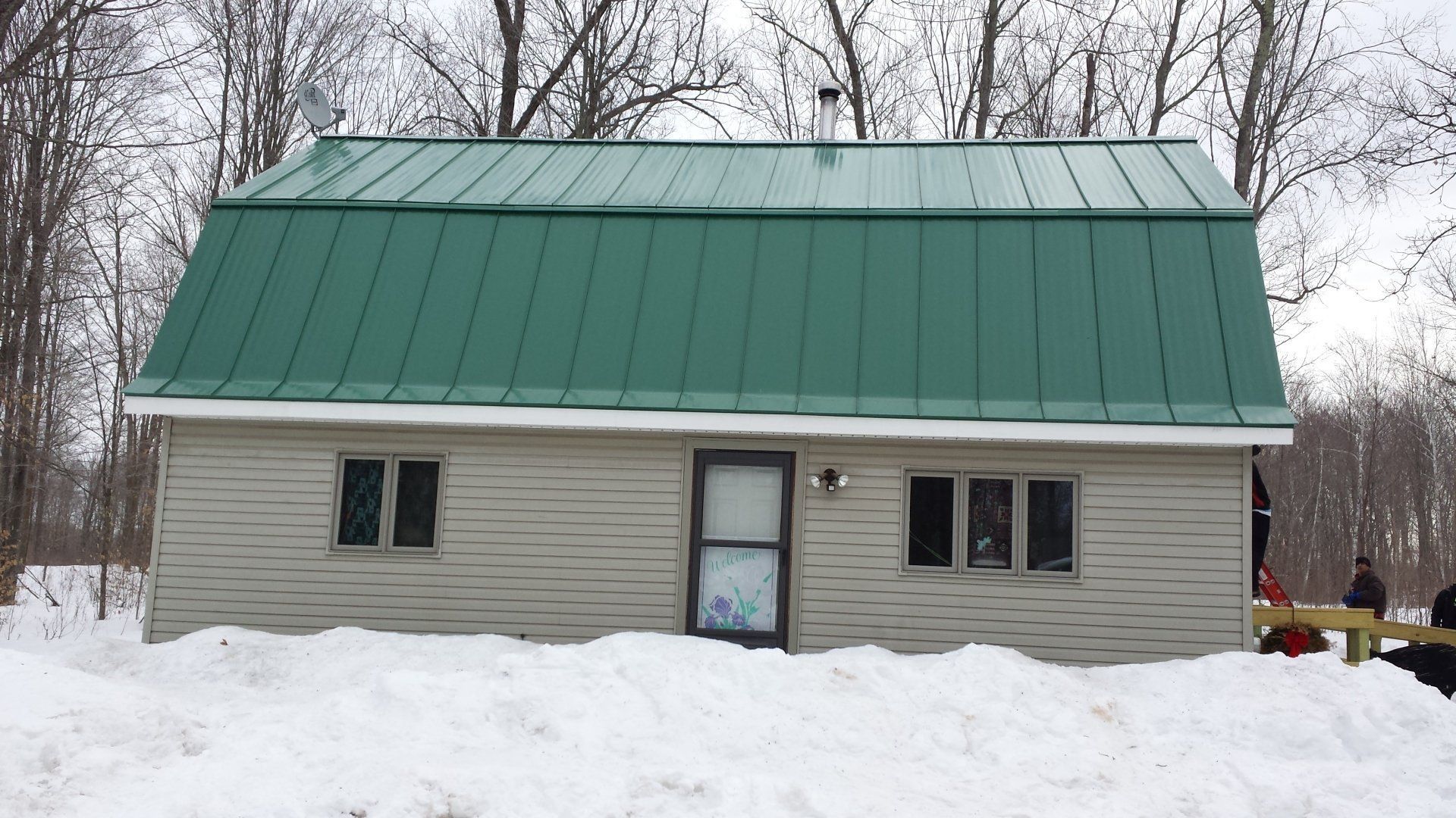 Small gray house with a green metal roof surrounded by snow and bare trees