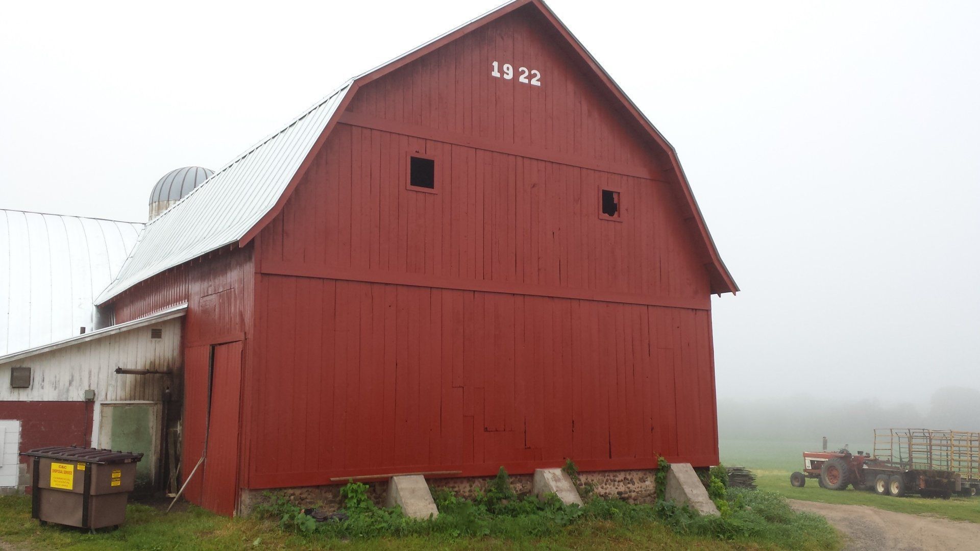 Red barn with white roof and the number 1928, standing in a foggy field.