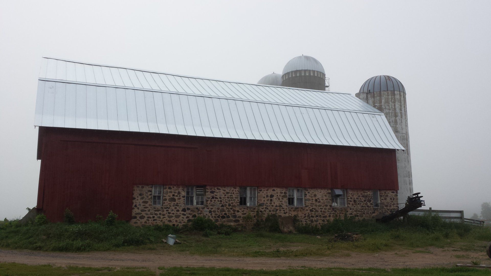 Red barn with a white roof and silos in a foggy rural field