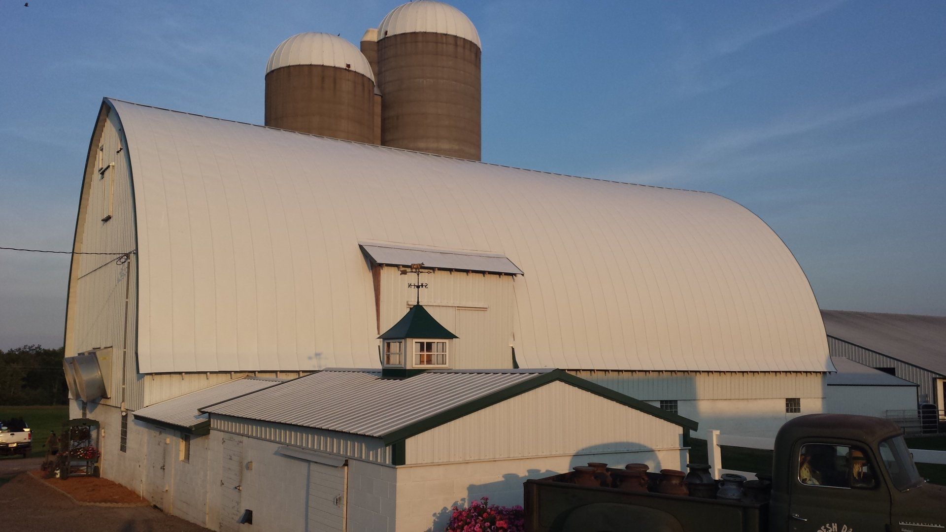 White barn with curved roof and twin silos on a farm under a clear sky
