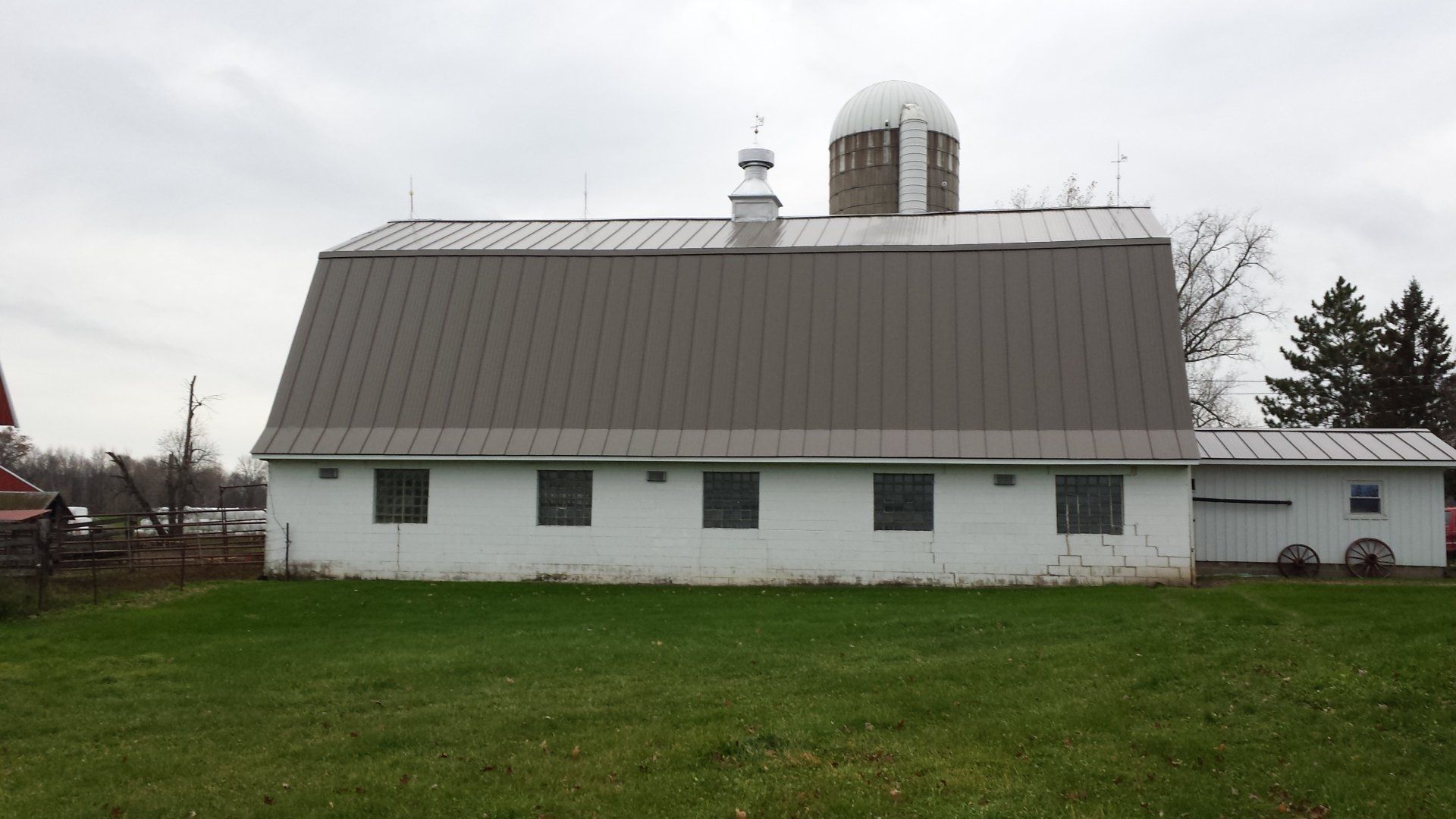 White barn with a gray roof and silo on a grassy field under an overcast sky