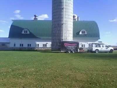 White barn with green roof and silo on grassy field, with two trucks parked in front.