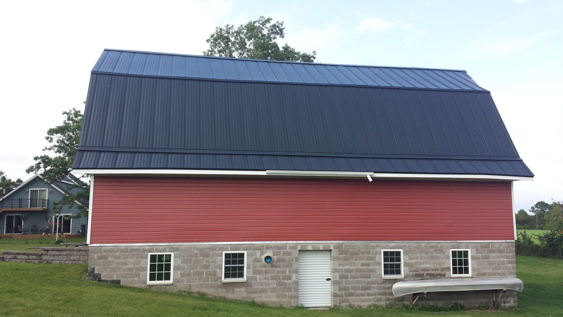 Red barn with a dark blue roof and stone foundation in a grassy rural setting.