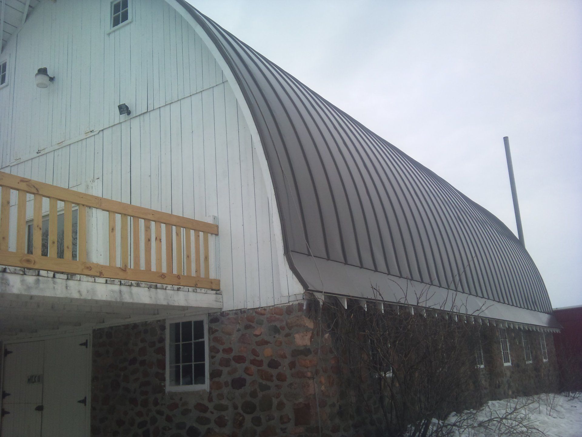 Curved white barn roof with stone base and small wooden balcony