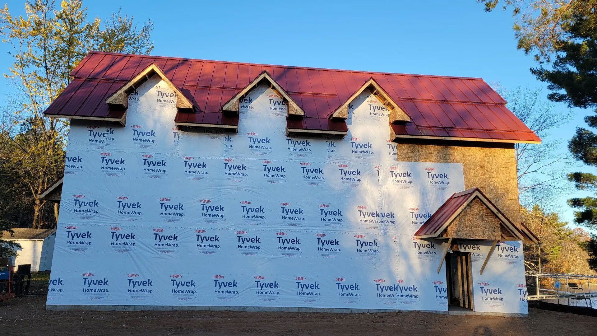 House under construction with white wrap, red roof, and small front porch in daylight