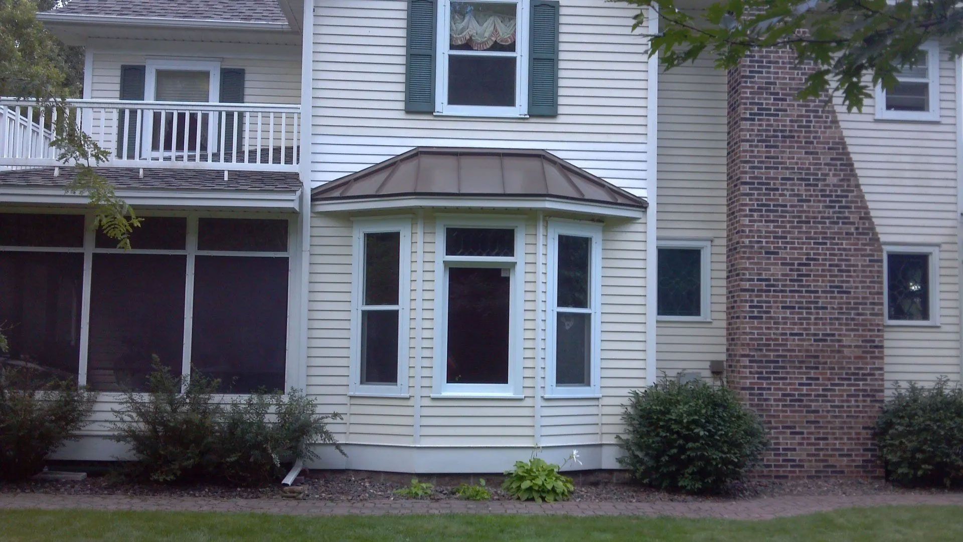 Residential house exterior with white siding, brick column, balcony, and bay windows