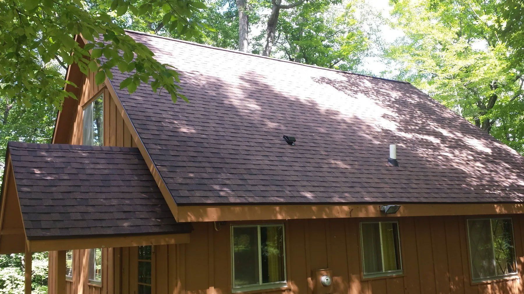 Wooden cabin with a steep shingled roof and trees casting dappled shade on the front