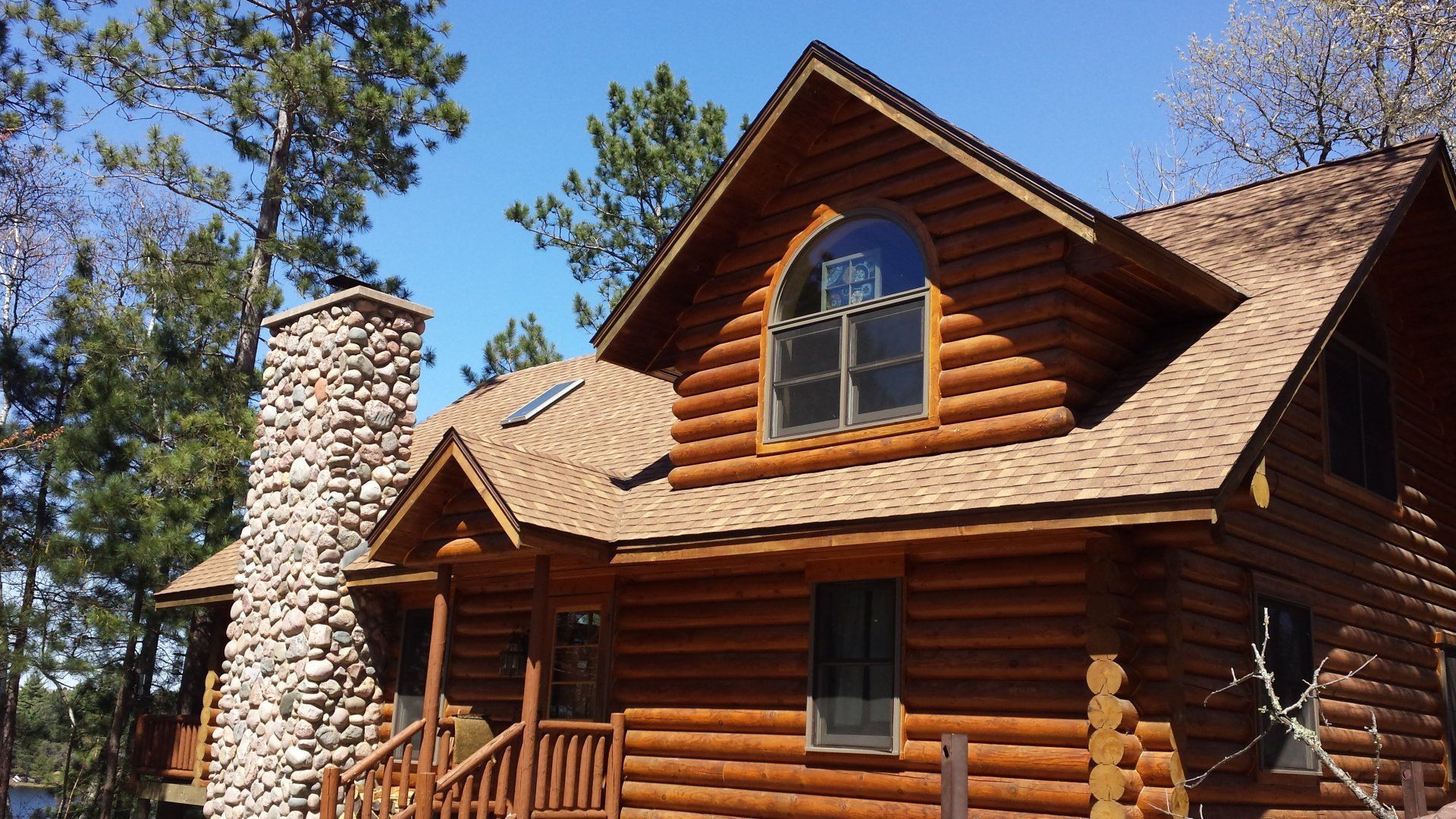 Rustic log cabin with stone chimney under blue sky and tall pine trees