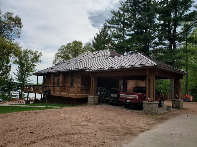 Log cabin-style house with a metal roof, porch, and red truck in a wooded lakeside setting