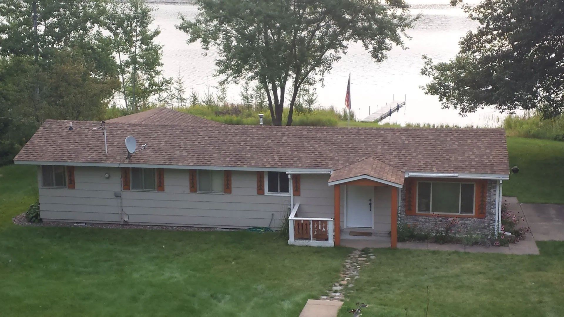 Single-story gray house with red-brown roof and front porch, set on a grassy lawn with trees behind.