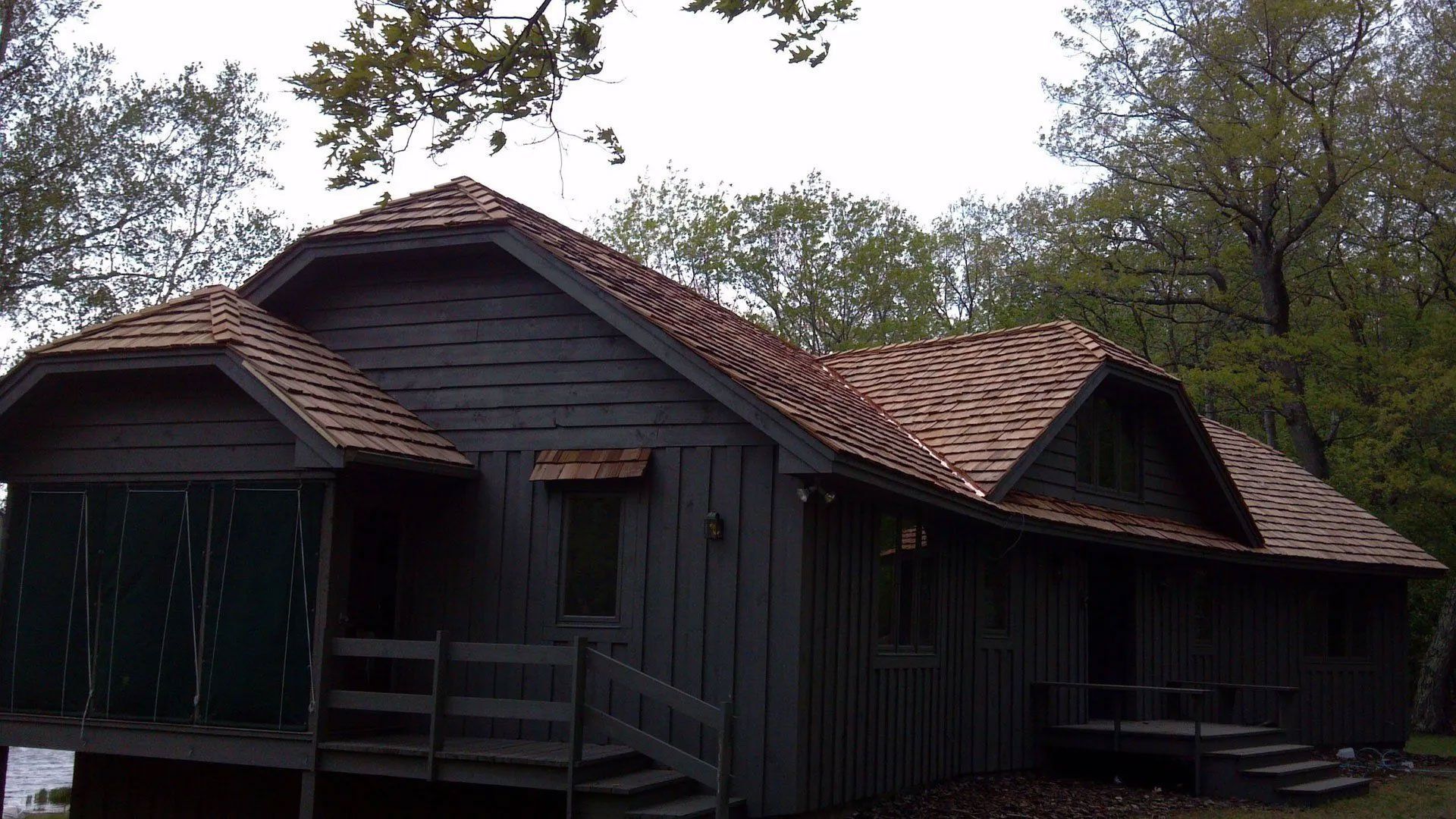 Dark wooden cabin with red-tile roofs in a wooded setting