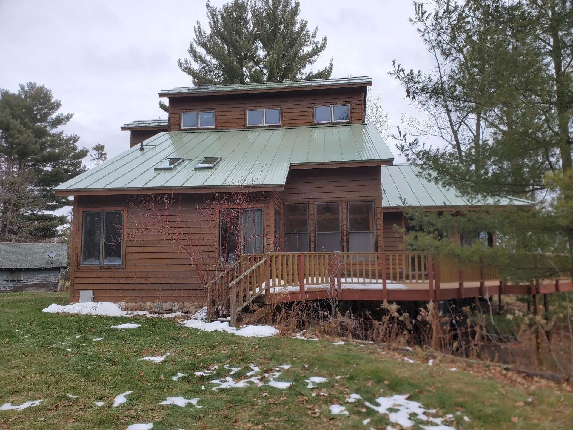 Rustic log cabin with green metal roof and wooden deck in a snowy wooded yard