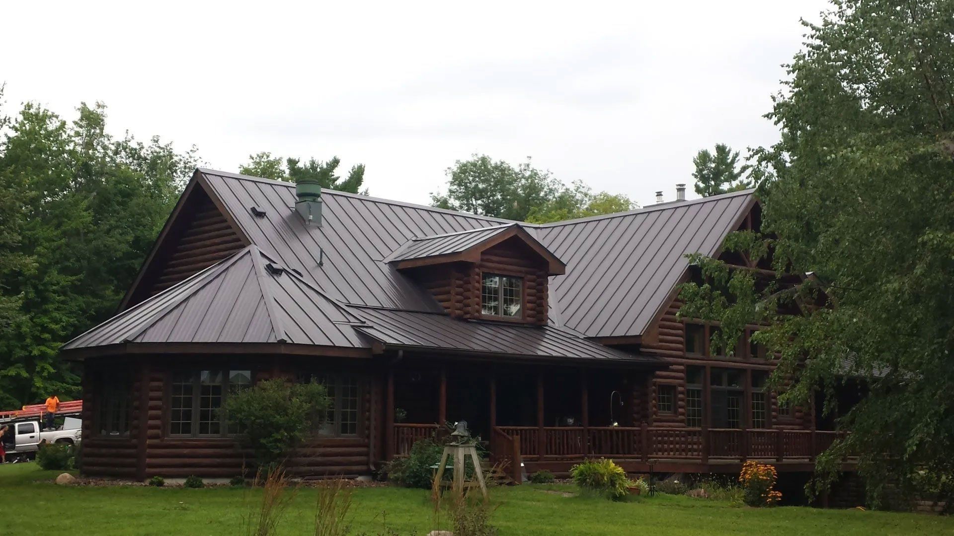 Dark wooden cabin with a gray metal roof surrounded by trees and grass