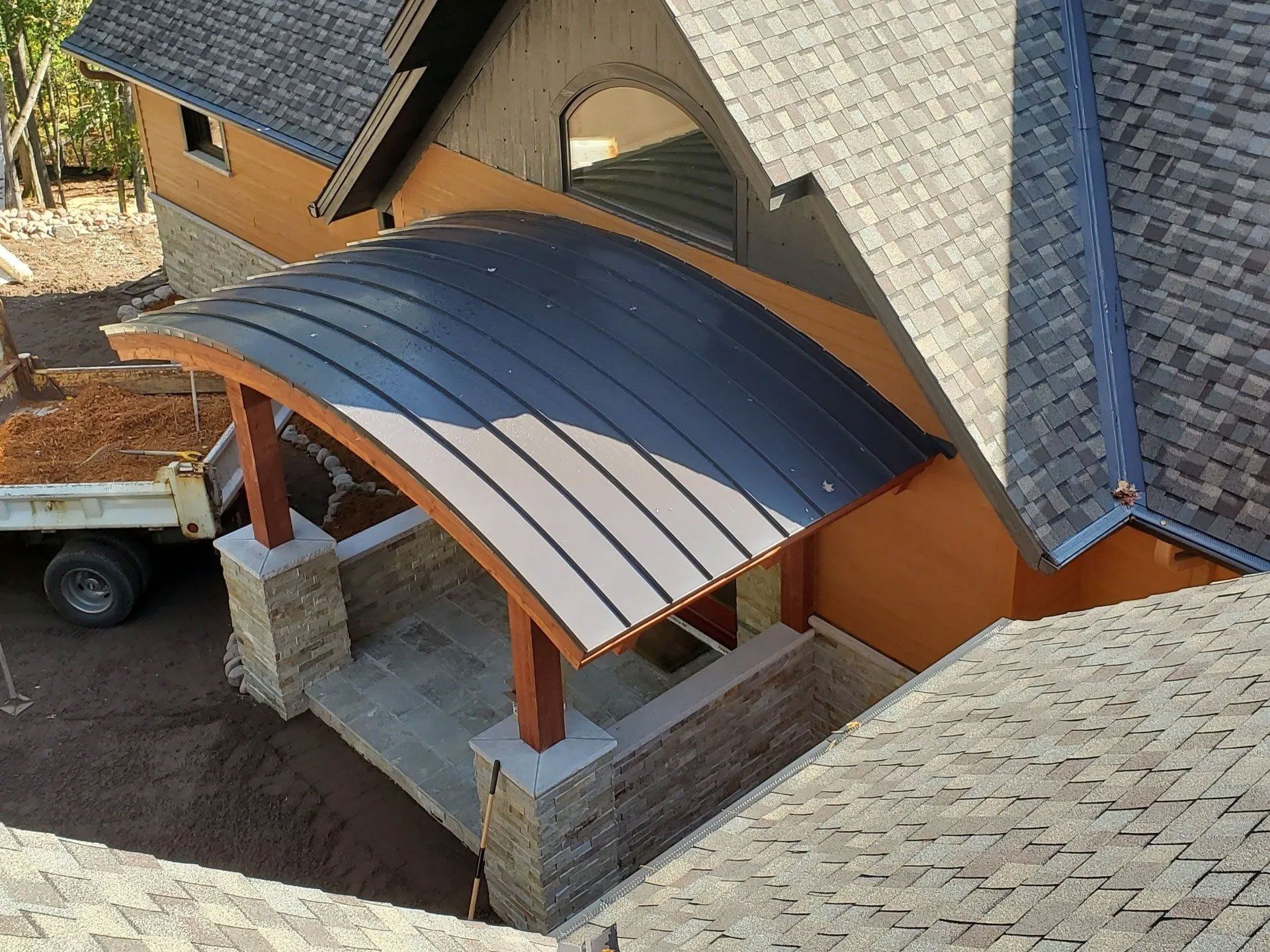 Roofed porch with dark metal canopy attached to a house with gray shingle roof and stone columns