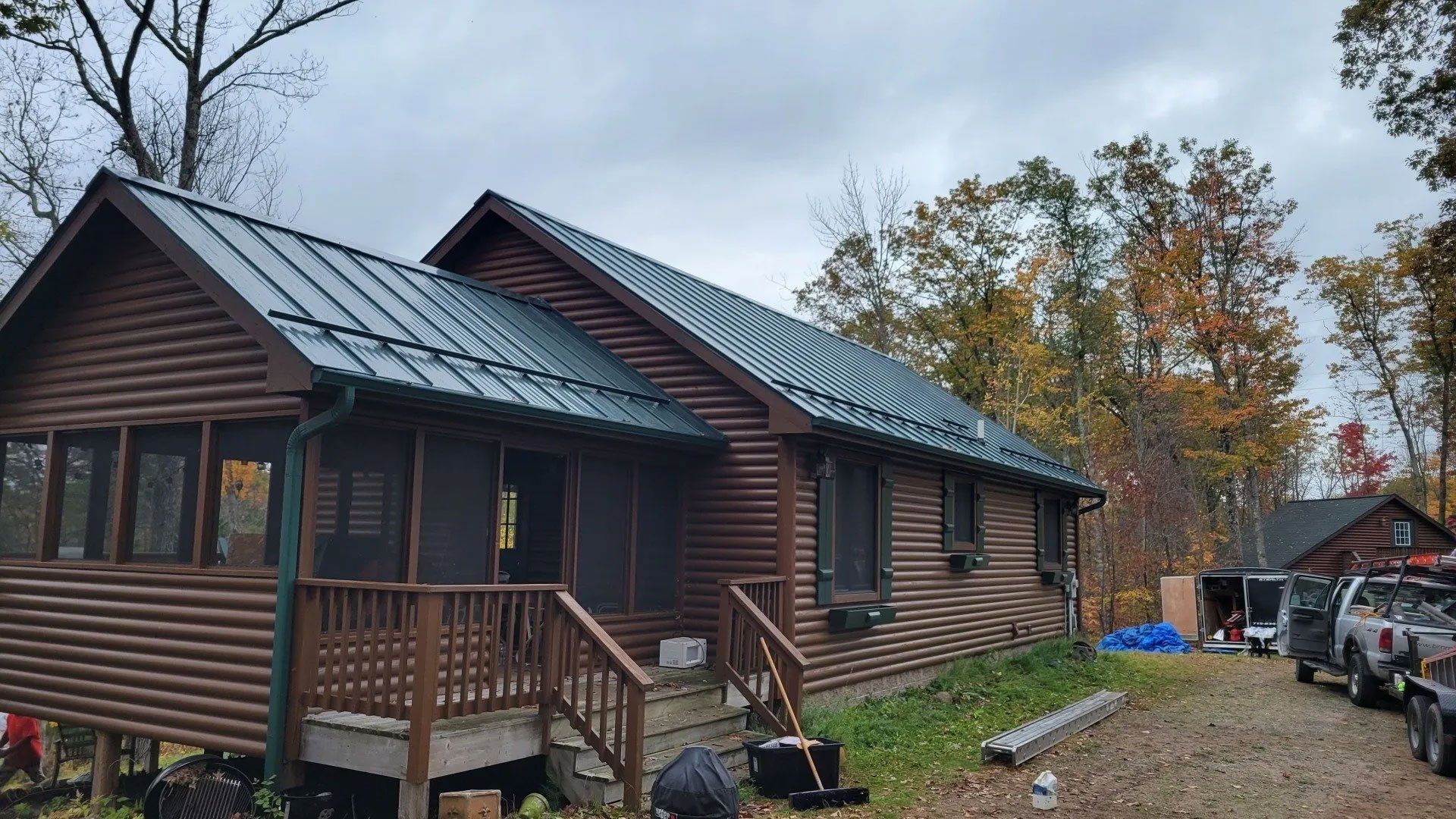 Two brown log cabins with green roofs beside a gravel driveway in autumn.