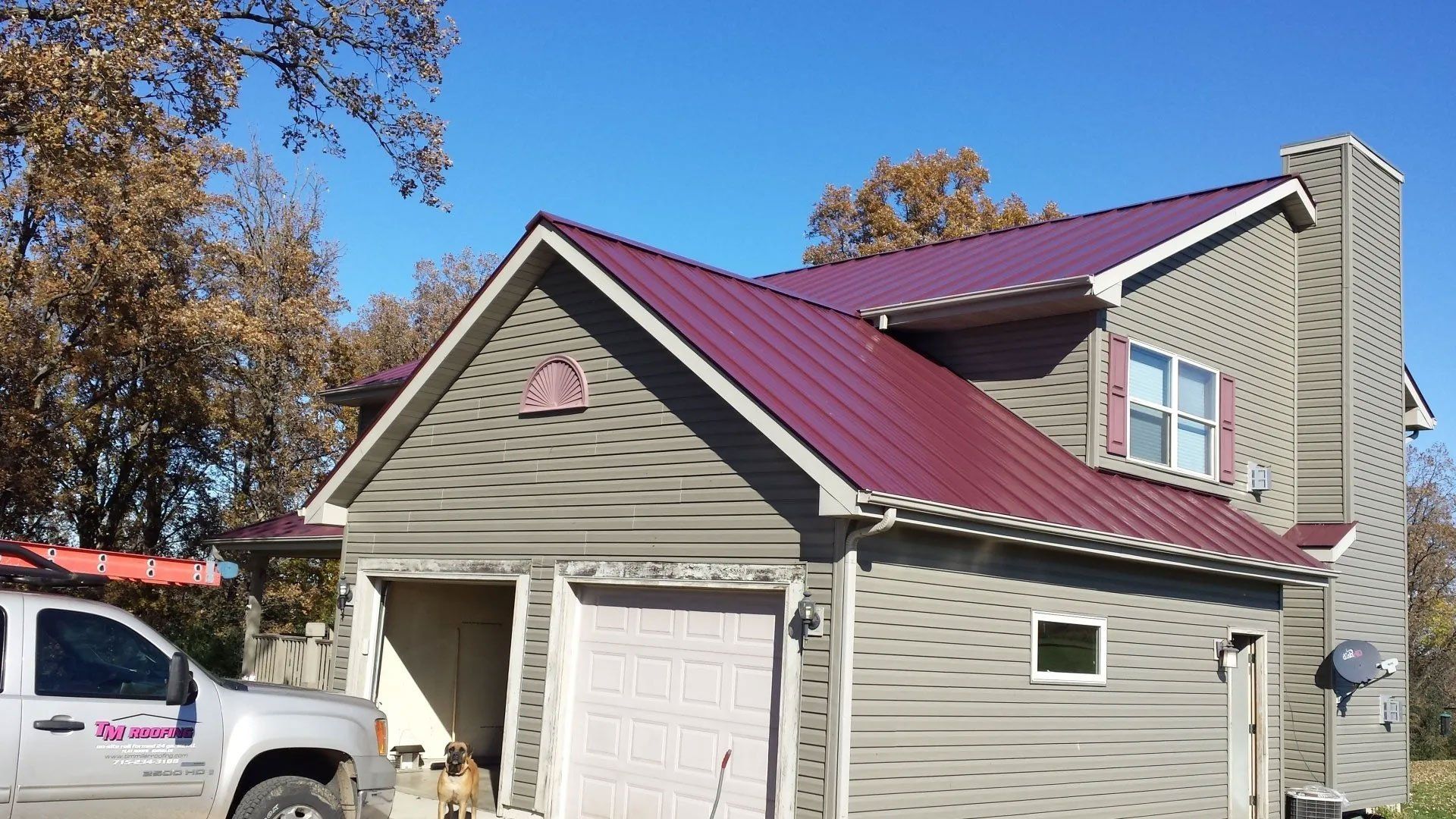 Gray house with maroon roof and white garage, viewed from the driveway under a clear blue sky