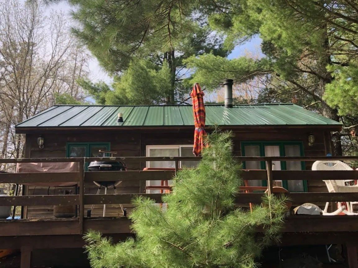 Cabin with green metal roof and wooden deck, surrounded by trees and a hanging red ornament