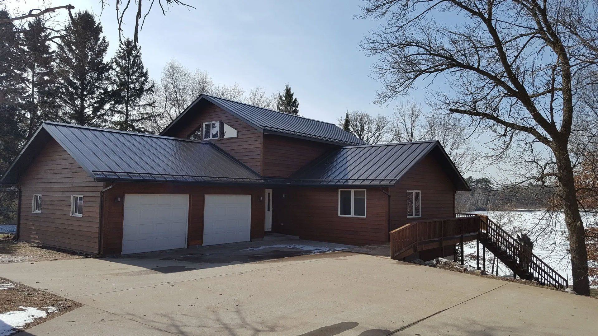 Brick house with double garage beside a snowy lake under bare trees and a clear sky